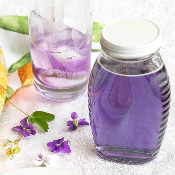 jar of violet syrup with some in glass too