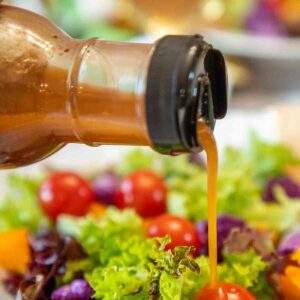 pouring sun dried tomato vinaigrette over salad